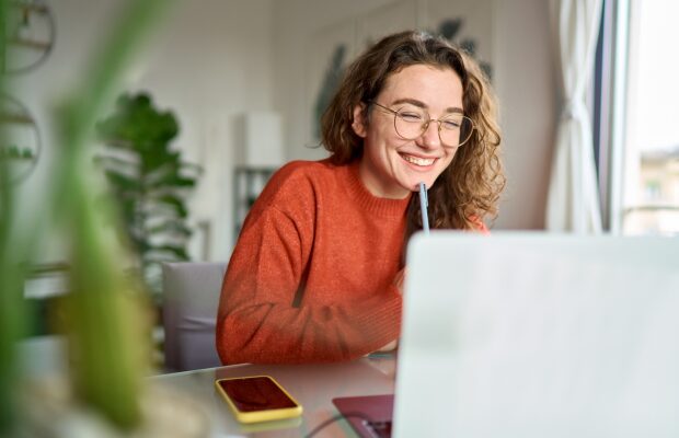 Girl in her home smiling whilst researching on laptop